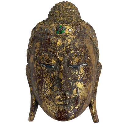 Frontaanzicht van het antieke Birmaanse giltwood Boeddhavoorhoofd met fijn handgeschilderd lijnwerk op de neergeslagen ogen en een groene Hmankazi glasrozet op de pata-band.