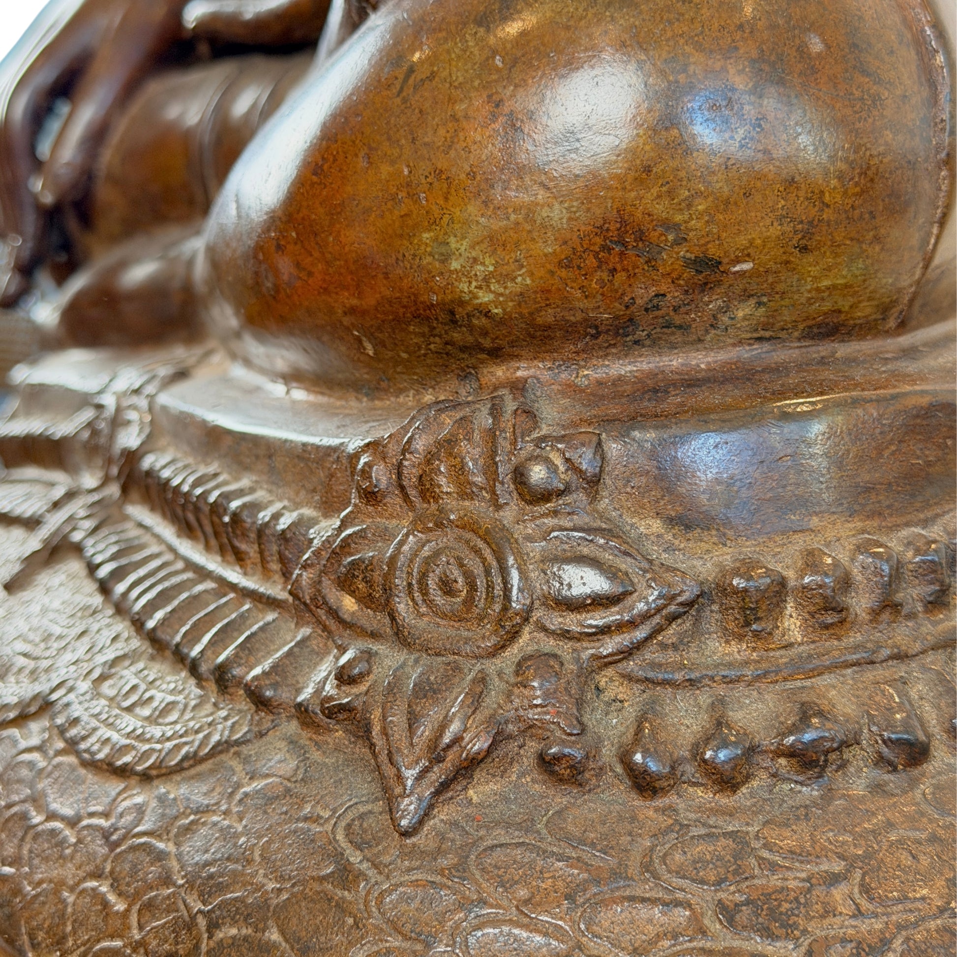 Close-up van het fijne giet- en etswerk op de troonbasis van een groot antiek Thais bronzen Boeddhabeeld, met focus op een bloemmotief en de natuurlijke goudbruine patina