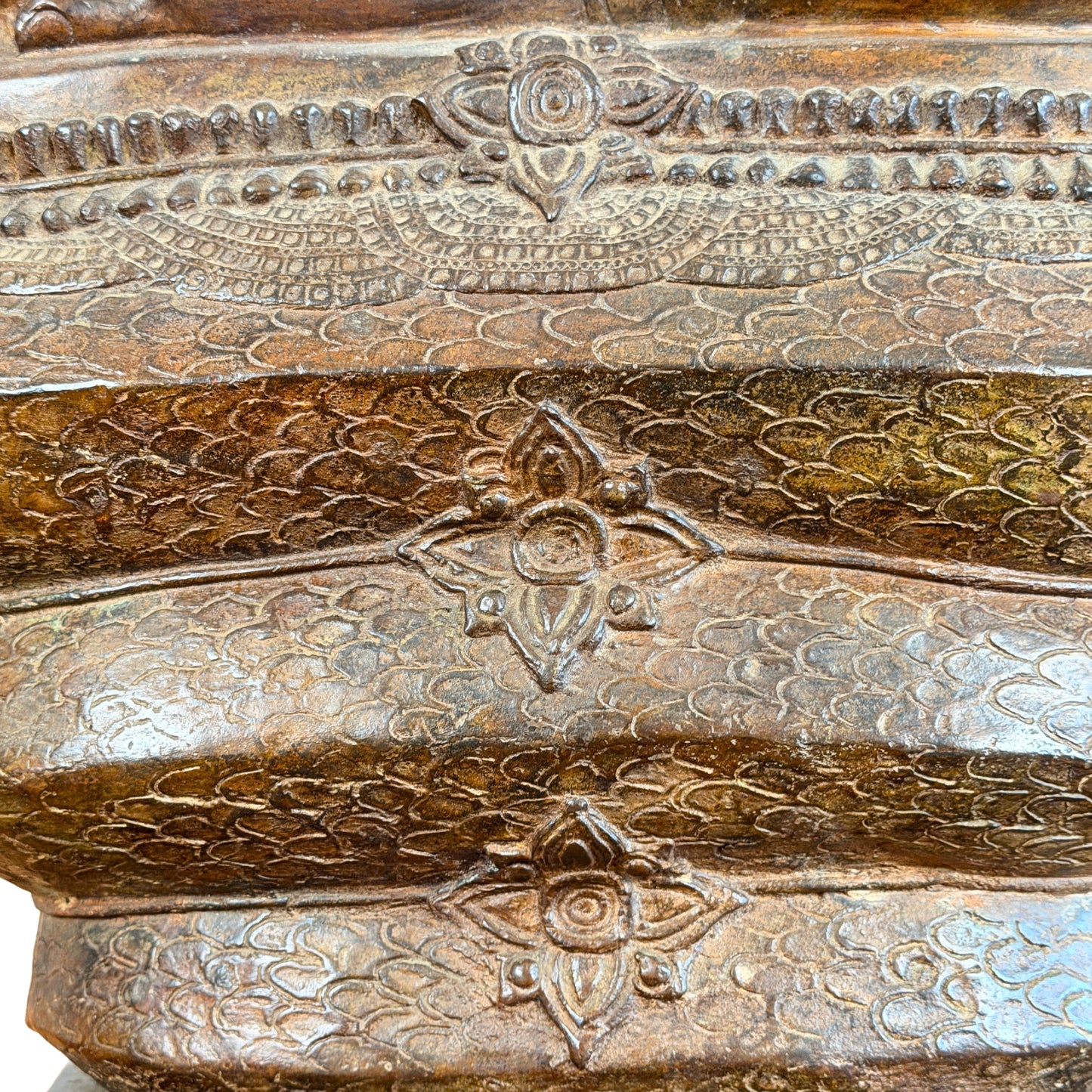 Close-up van de rijk gedecoreerde slangenwindingen van een antiek Thais bronzen Boeddhabeeld, met een gedetailleerd patroon van slangenschubben en decoratieve reliëf-bloemen in een warme bruine patina.