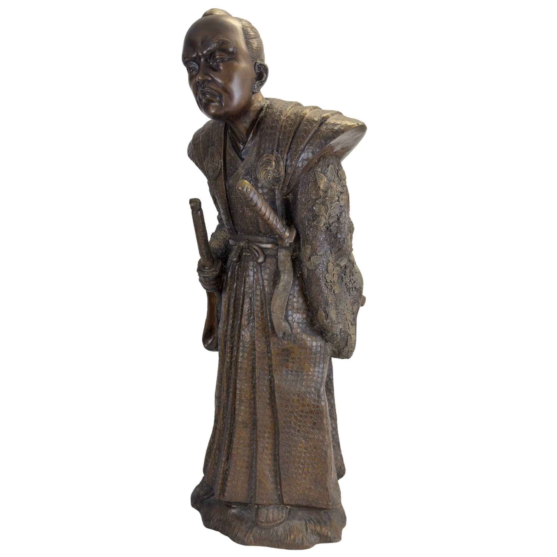 Driekwart vooraanzicht van de bronzen Samurai in zijn ceremoniële krijgshouding met de Daisho-zwaarden prominent zichtbaar.