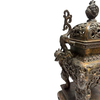 Sfeervolle detailopname van het linker handvat in de vorm van een klimmende draak en het diepe reliëf op de hoek van de bronzen brander.
