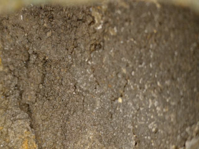 Microscoopdetail van korrelige oude gietkern en ruwe bronzen binnenwand