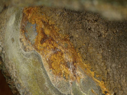 Microscoopdetail van oranjebruine oxidatie langs de overgang van gietkern naar brons
