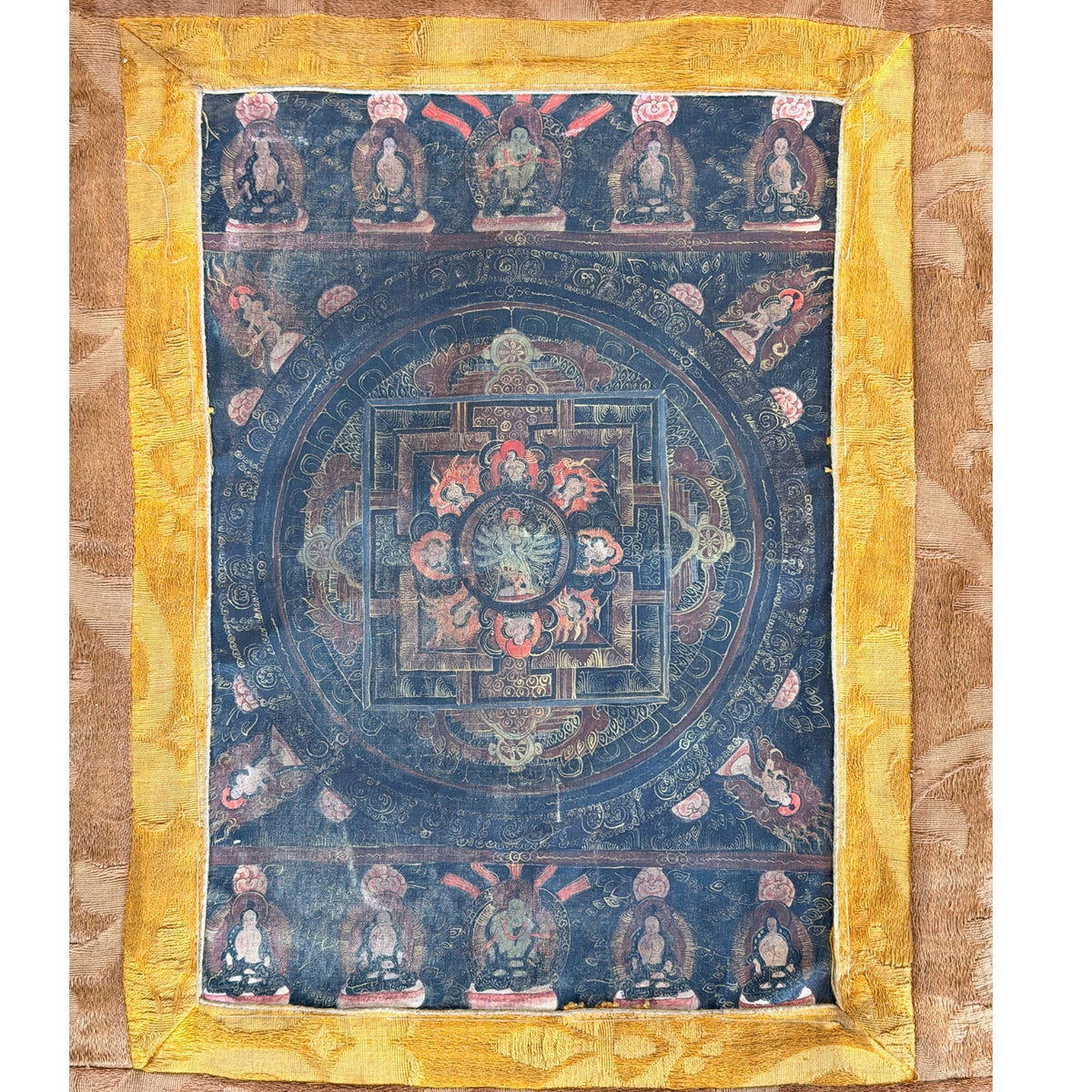 Schilderijveld van de mandala-thangka binnen de gele zijden rand, met een rij zittende figuren boven en onder