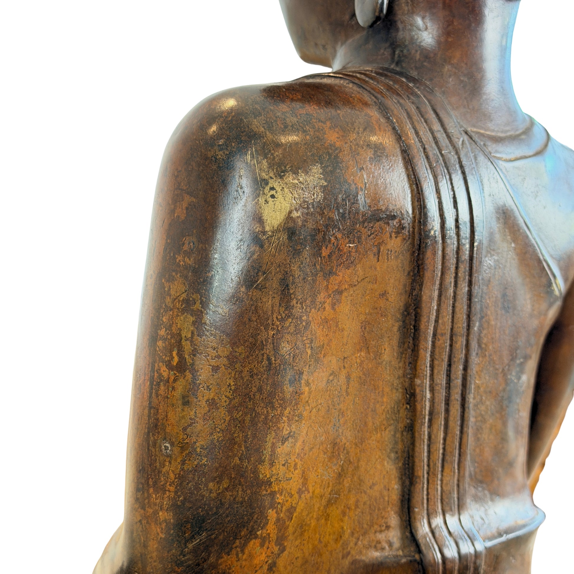Macro-opname van de rechterschouder aan de achterzijde van een bronzen Boeddhabeeld, tonende de verticale plooien van het monnikskleed en een blootgelegde zone met originele goudgrijze vuurvergulding onder de verweerde bruine patina