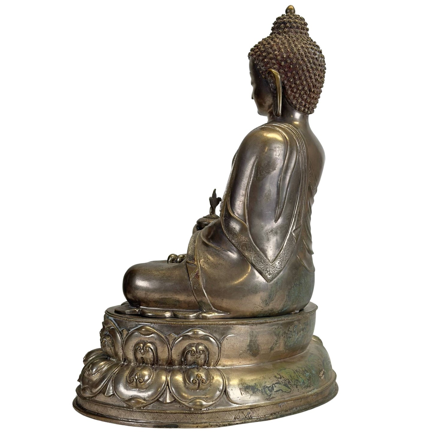 Linkerzijde van een antieke Newar Bhaisajyaguru in verzilverd brons op een tweedelige lotustroon, met natuurlijke patina, gegraveerde monnikspij en slijtage passend bij hoge ouderdom.