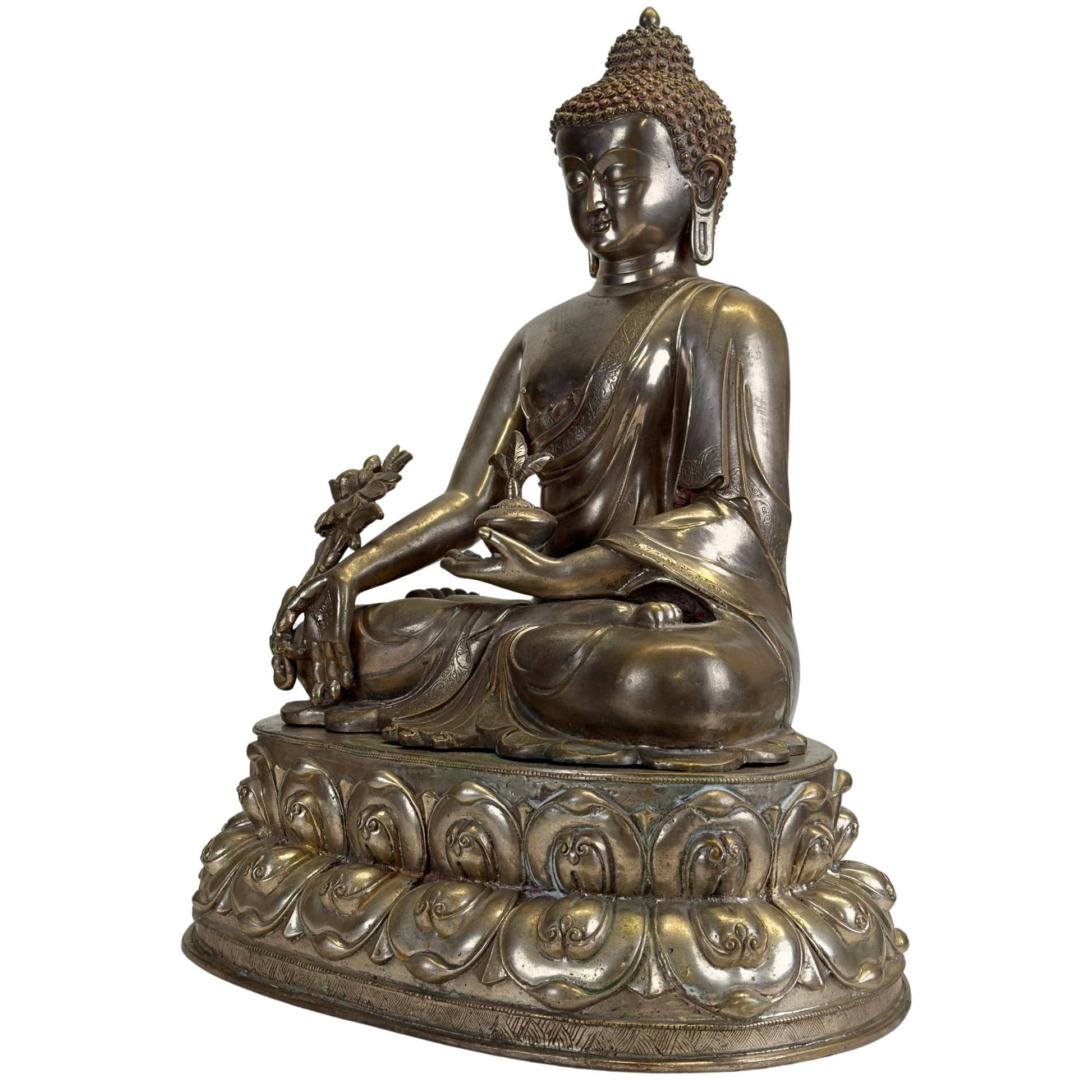 Schuin vooraanzicht van een antieke Newar Bhaisajyaguru in verzilverd brons met medicijnpot, grote myrobalanplant, fijn gegraveerde gewaden, tweedelige lotustroon en natuurlijke patina.