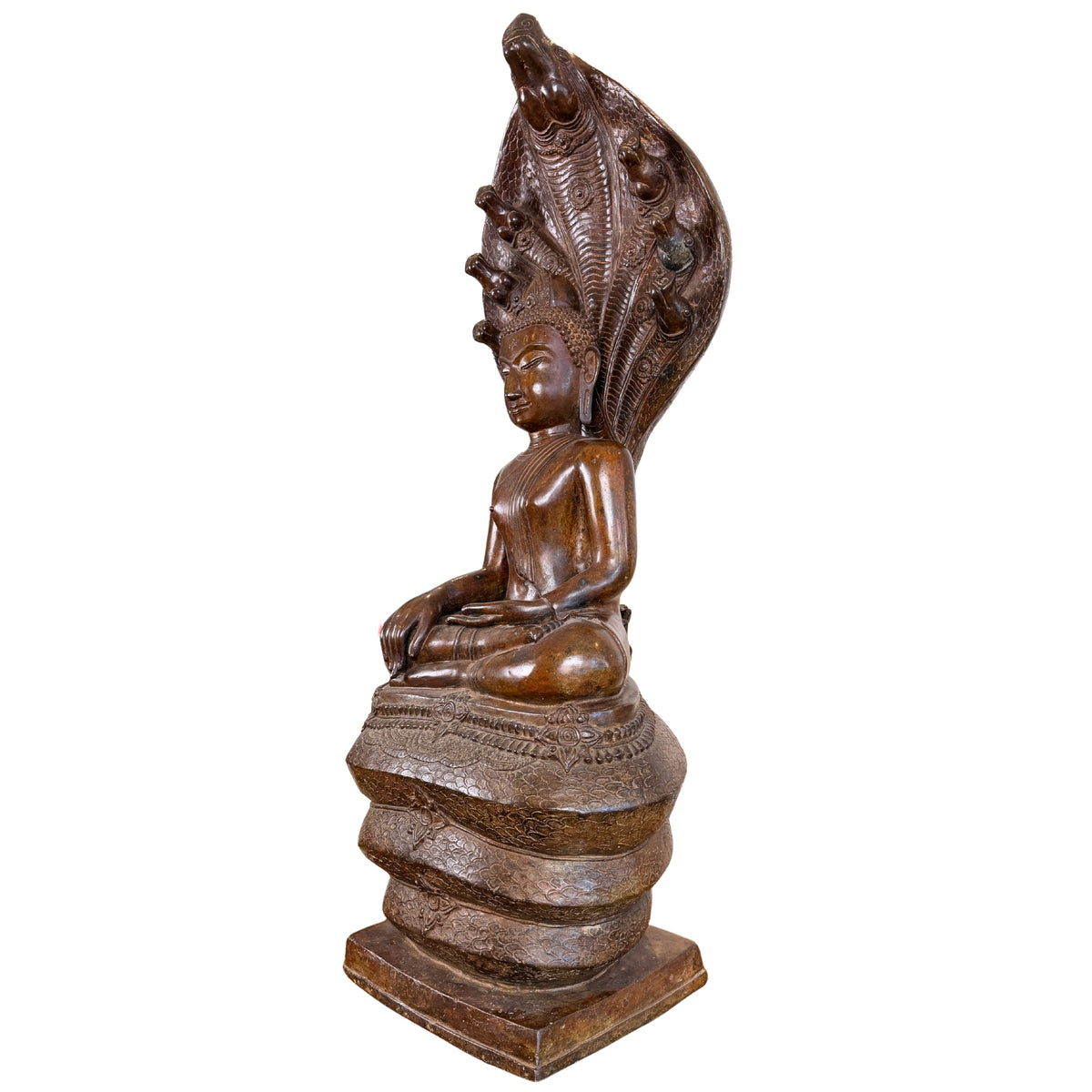 Zijaanzicht in driekwart profiel van een monumentaal bronzen Phra Nagprok Boeddhabeeld van 122 cm hoog, tonende de zittende figuur op de opgerolde naga-windingen onder het imposante, opwaartse scherm van de zevenkoppige Naga-slang.