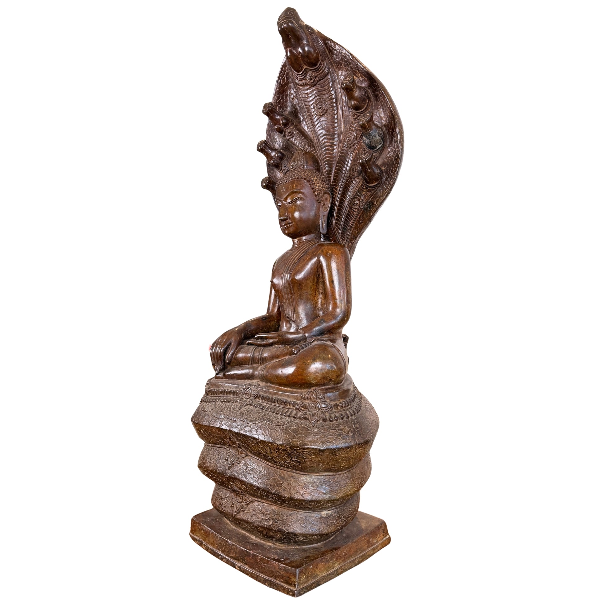 Zijaanzicht in driekwart profiel van een monumentaal bronzen Phra Nagprok Boeddhabeeld van 122 cm hoog, tonende de zittende figuur op de opgerolde naga-windingen onder het imposante, opwaartse scherm van de zevenkoppige Naga-slang.