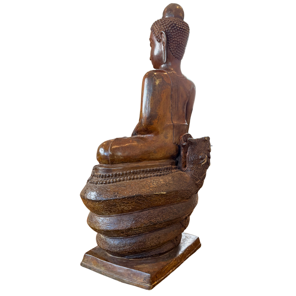 Schuin achteraanzicht van een monumentaal bronzen Boeddhabeeld van 122 cm hoog op de opgerolde naga-windingen, gefotografeerd zonder de afneembare kap waarbij de open penverbinding aan de achterzijde van de troon zichtbaar is