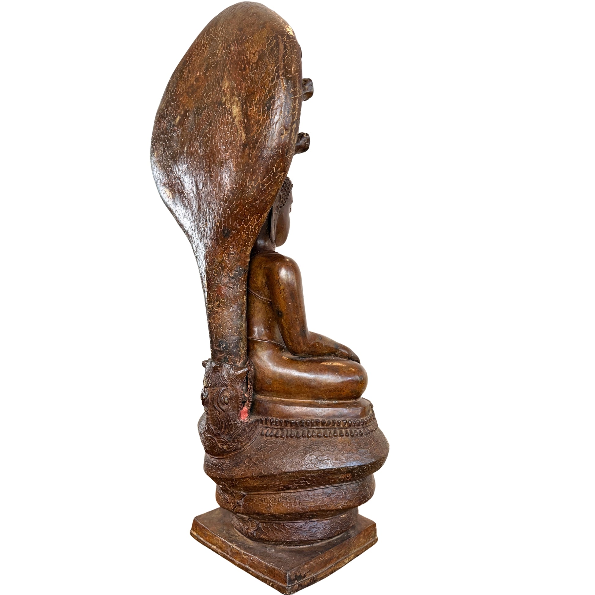 Schuin zijaanzicht van een monumentaal bronzen Phra Nagprok Boeddhabeeld in Grahi-stijl, tonende de zittende Boeddha op de slangentroon onder het grote zevenkoppige slangenscherm dat is verankerd in de achtste slangenkop aan de achterzijde
