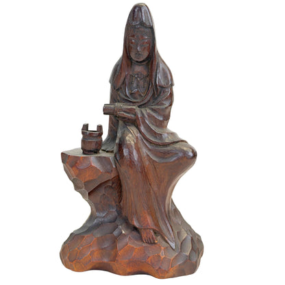 Vooraanzicht van de handgesneden Japanse houten Kannon (Guanyin) zittend op een rotsbasis met een offervat in kastanjebruine patina.