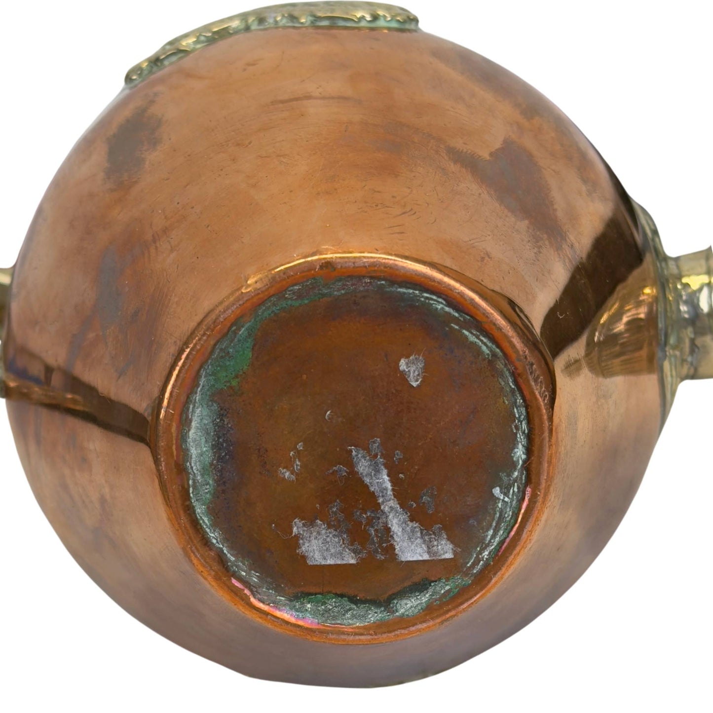 Direct onderaanzicht van de theepot, tonend de messing standring met groene verdigris-buildup en witte papierlijmresten in het centrum.